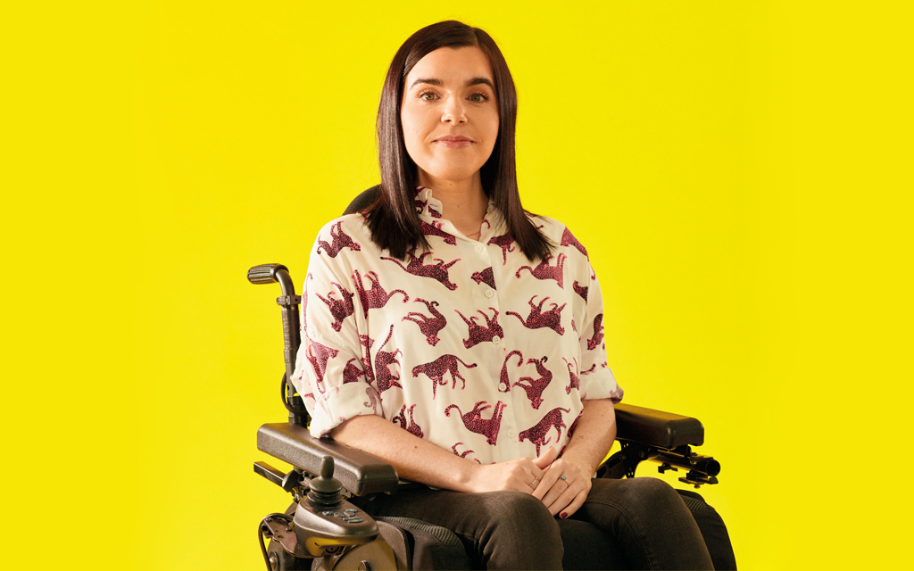 Emma Muldoon seated in her wheelchair in front of a yellow background.